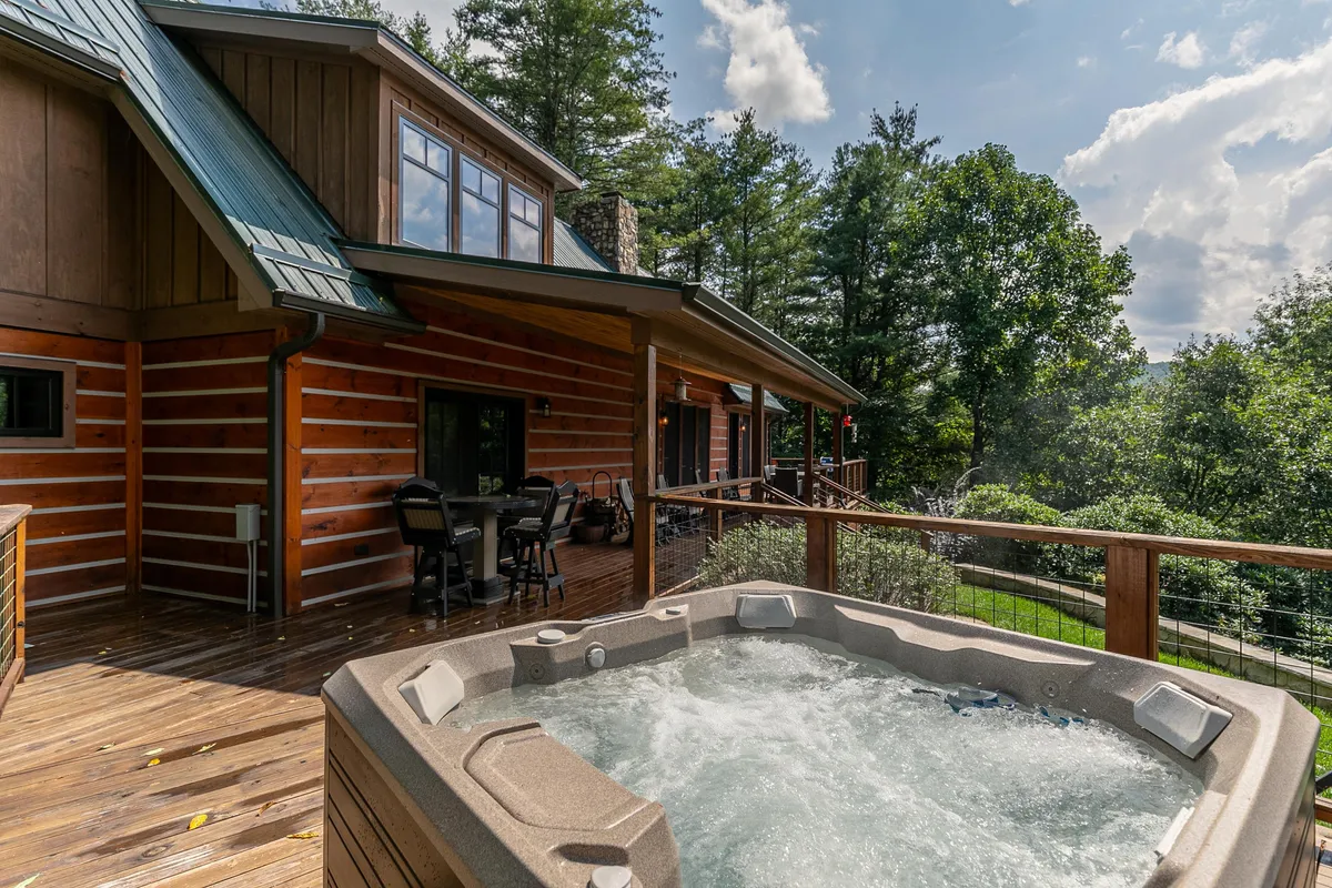 A deck area with a hot tub, dining table, and seating, all framed by surrounding trees. The space is ideal for both soaking in the hot tub and enjoying outdoor meals, with a relaxed, rejuvenating mood and a clear connection to nature.