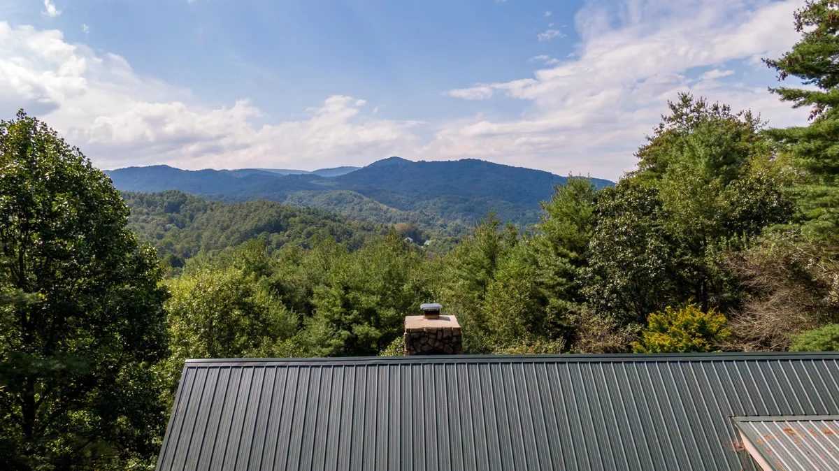 A panoramic view of a mountain range blanketed by dense trees under a clear blue sky. The foreground hints at open spaces perfect for picnicking, hiking, or simply soaking in the scenery. The mood is serene and adventurous, evoking the essence of mountain exploration.