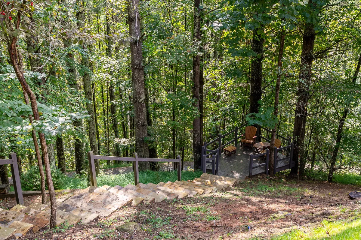 The photo features wooden stairs leading to a cozy seating area on a deck, surrounded by vibrant trees. The setting evokes relaxation, autumn foliage walks, stargazing from the deck, and summer barbecues in nature.