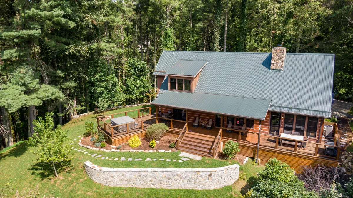 A wide view of a wooden deck overlooking a lush green lawn bordered by mature trees, with a stone pathway leading into the natural landscape. The deck is ideal for barbecues, outdoor dining, and soaking in sunset views, and the open lawn invites group activities and relaxation.
